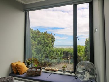 A seating area with cushions plants and a fan by a large window with a view of greenery and the sea at Sunriser in Tara Hill near Ballymoney County Wexford