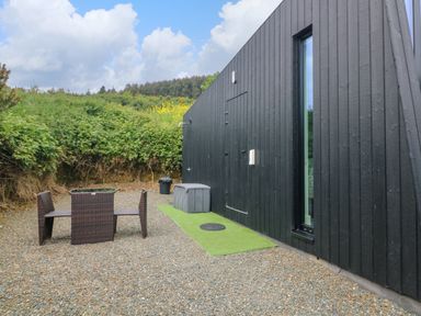 An outdoor area with a black wooden building a glass table and two chairs on gravel at Sunriser in Tara Hill near Ballymoney County Wexford