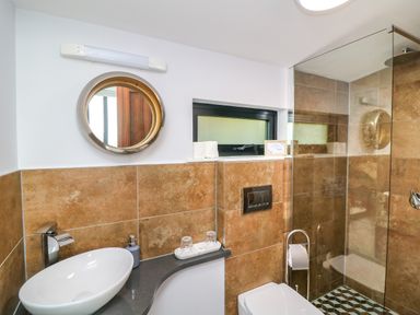 A bathroom with a round mirror above a sink and a glass shower at Sunriser in Tara Hill near Ballymoney County Wexford