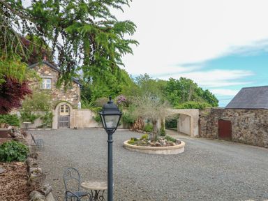 A gravel courtyard with a round garden bed a stone building and a lamp post at Sunriser Tara Hill near Ballymoney County Wexford