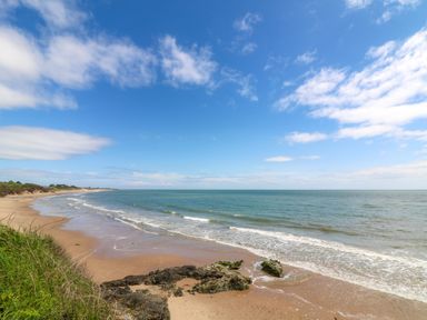 A sandy beach with rocks and grassy dunes beside the ocean under a blue sky at Sunriser in Tara Hill near Ballymoney County Wexford