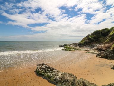 A sandy beach with rocks and vegetation near the shore under a partly cloudy sky at Sunriser in Tara Hill near Ballymoney County Wexford