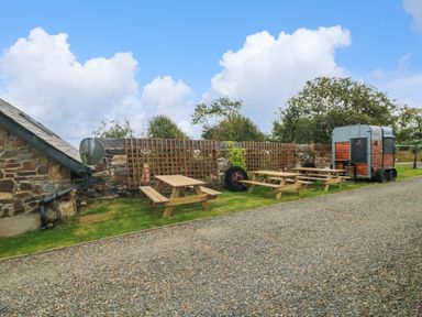 An outdoor area with picnic tables a stone wall a small building with a satellite dish and a wooden trailer at Sunriser in Tara Hill near Ballymoney County Wexford