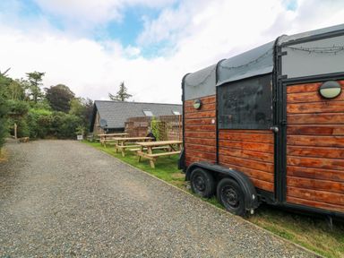 An outdoor area with picnic tables on grass and a wooden trailer beside a gravel path at Sunriser in Tara Hill near Ballymoney County Wexford
