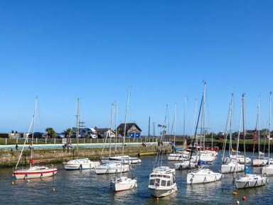 A harbor with sailboats anchored in the water near a stone wall with cars and buildings in the background at Sunriser in Tara Hill near Ballymoney County Wexford