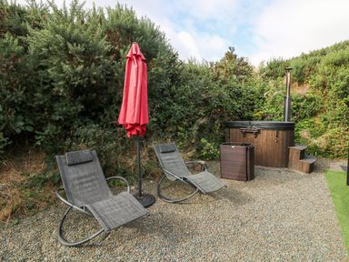 Two lounge chairs with a closed red umbrella and a wooden hot tub in a garden at Sunriser Tara Hill near Ballymoney County Wexford