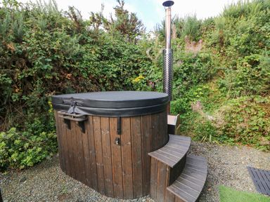 An outdoor wooden hot tub with a cover and steps surrounded by bushes at Sunriser in Tara Hill near Ballymoney County Wexford
