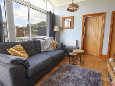 A living room with a gray sofa with cushions a floor lamp wooden nested tables and a large window at Pebble Beach Chalet in Seaton