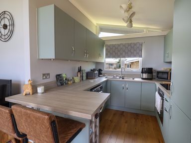 A kitchen with light blue cabinets wooden floor and a countertop with two brown stools at Pebble Beach Chalet in Seaton