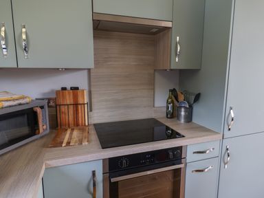 A kitchen countertop with a microwave, wooden cutting boards, stove, oven, utensils and cabinets at Pebble Beach Chalet in Seaton