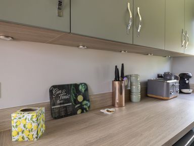 A kitchen countertop with a tissue box, cutting board, knife holder, stacked cups, toaster, and coffee machine at Pebble Beach Chalet in Seaton