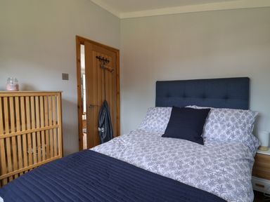A bedroom with a bed with patterned bedding and a dark pillow a wooden door with hangers and a wooden dresser at Pebble Beach Chalet in Seaton