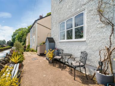 An outdoor patio area with two black cushioned chairs and a small round table next to a white textured wall at Holly Cottage in Great Malvern
