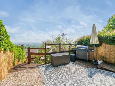 An outdoor deck area with a barbecue grill umbrella storage box and a view of the countryside at Holly Cottage in Great Malvern