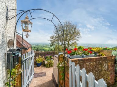 A garden entrance with a blue gate flowers in pots and a countryside view at Holly Cottage in Great Malvern