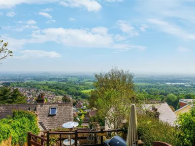 A residential hillside view with rooftops trees and fields under a blue sky in Great Malvern