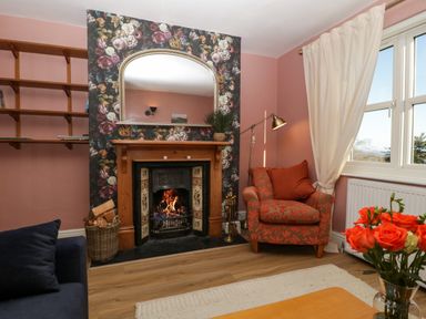 A living room with a fireplace an armchair a window and a bouquet of orange roses at Holly Cottage in Great Malvern