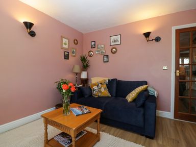 A living room with a blue sofa and cushions next to a wooden coffee table with flowers in a vase on it at Holly Cottage in Great Malvern