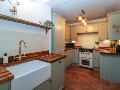 A kitchen with wooden countertops a white sink a stove and cabinets at Holly Cottage in Great Malvern