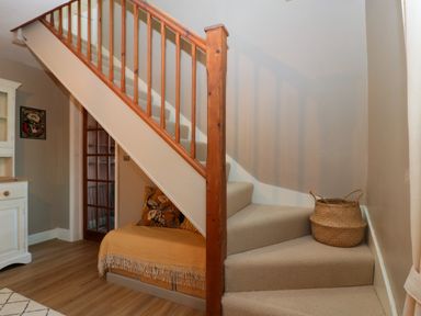 A staircase with carpeted steps and wooden banister next to a bench with cushions and a basket on the steps at Holly Cottage in Great Malvern