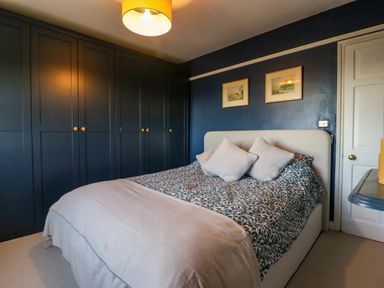 A bedroom with a double bed pillows large dark wardrobes and framed pictures on the wall at Holly Cottage in Great Malvern