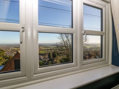 A paneled window overlooking houses trees and open countryside at Holly Cottage in Great Malvern