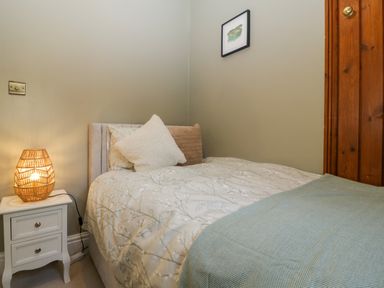 A bedroom with a single bed white nightstand with lamp and framed picture on wall at Holly Cottage in Great Malvern