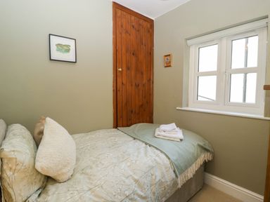 A small bedroom with a bed a window and a wooden door at Holly Cottage in Great Malvern