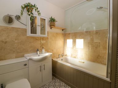 A bathroom with a bathtub a sink under a mirrored cabinet and two plants at Holly Cottage in Great Malvern