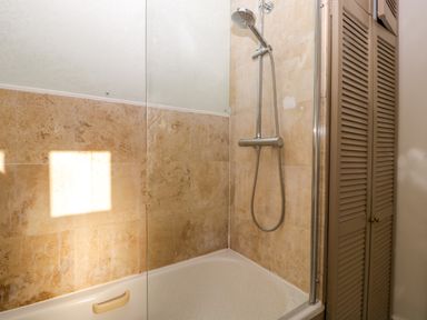 A bathroom with a showerhead above a bathtub and tiled walls next to a louvered door cupboard at Holly Cottage in Great Malvern