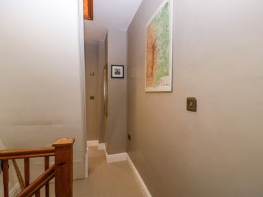A narrow upstairs hallway with a wooden banister a framed map and picture on the walls at Holly Cottage in Great Malvern