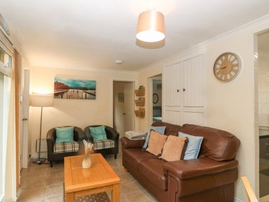 A living room with a brown leather sofa pillows two black armchairs wooden coffee table and wall clock at 245 Riverside Lodge in Caeathro