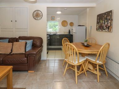 A dining area with wooden table and chairs next to a kitchen and a brown leather sofa with cushions at 245 Riverside Lodge in Caeathro