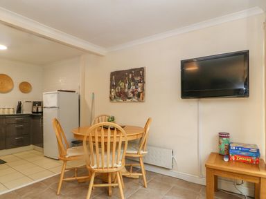 A dining area with wooden table and chairs next to a wall-mounted TV and a small side table with board games at 245 Riverside Lodge in Caeathro