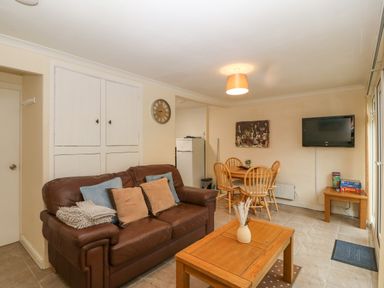 A living room with a brown leather sofa cushions wooden coffee table and dining table with chairs at 245 Riverside Lodge in Caeathro