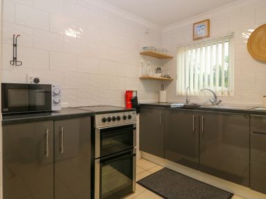 A kitchen with black cabinets appliances a microwave oven a sink and a window at 245 Riverside Lodge in Caeathro