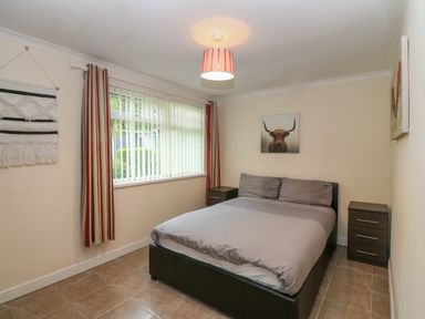 A bedroom with a bed two bedside tables striped curtains and a window at 245 Riverside Lodge in Caeathro