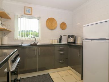 A kitchen with gray cabinets a window above the sink a refrigerator and kitchen appliances at 245 Riverside Lodge in Caeathro