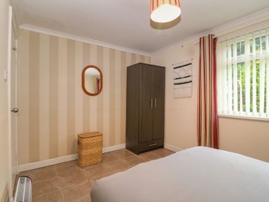 A bedroom with striped wallpaper a dark wardrobe wicker basket and a window with vertical blinds and striped curtains at 245 Riverside Lodge in Caeathro