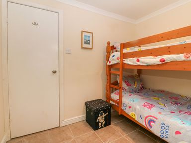 A small bedroom with wooden bunk beds and a storage box next to a closed door at 245 Riverside Lodge in Caeathro