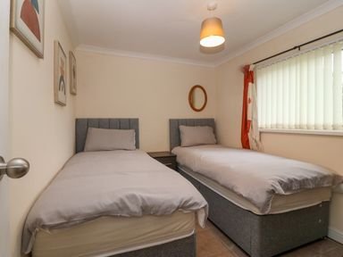 A bedroom with two single beds a nightstand between them wall art window with vertical blinds and a ceiling light at 245 Riverside Lodge in Caeathro