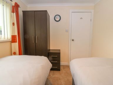 A bedroom with two beds a dark wardrobe a drawer unit and a wall clock at 245 Riverside Lodge in Caeathro