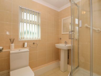 A bathroom with a toilet sink shower and a window with vertical blinds at 245 Riverside Lodge in Caeathro
