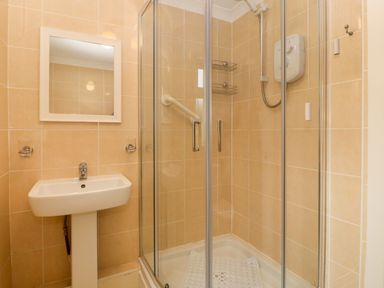 A bathroom with a pedestal sink and a glass-enclosed corner shower at 245 Riverside Lodge in Caeathro