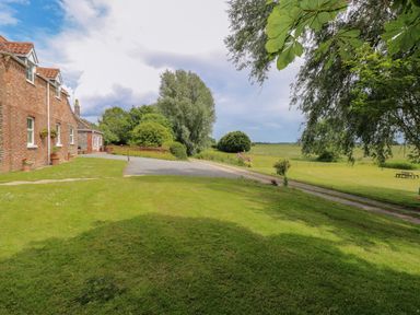A grassy yard with a brick house on the left trees flowers and a picnic table at Dairy Cottage in West Caister near Caister-on-Sea