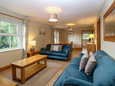 A living room with two blue sofas wooden coffee and side tables and a dining table in the background at Dairy Cottage West Caister near Caister-on-Sea