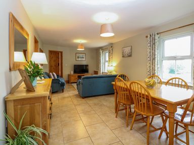 A living room with blue sofas a wooden dining table and chairs and a TV at Dairy Cottage in West Caister near Caister-on-Sea
