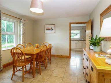A dining room with a wooden table and chairs next to a window and a wooden sideboard with a plant and lamp at Dairy Cottage in West Caister near Caister-on-Sea
