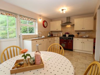 A kitchen with cream cabinets a red oven a round table with a floral tablecloth and a tray holding a flower bottle and papers at Dairy Cottage in West Caister near Caister-on-Sea