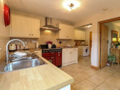 A kitchen with a sink, red oven, white cabinets, washing machine, and a wooden door at Dairy Cottage in West Caister near Caister-on-Sea